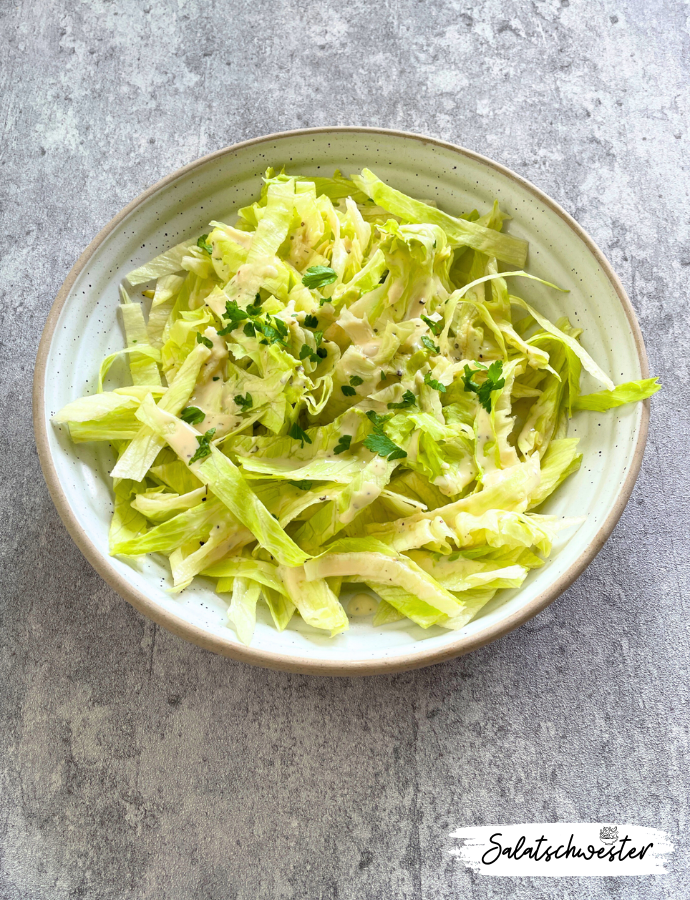 Frischer Eisbergsalat mit veganem Joghurt-Knoblauch-Dressing, angerichtet mit Kräutern auf einem weißen Teller – ideal als leichte Sommerbeilage.