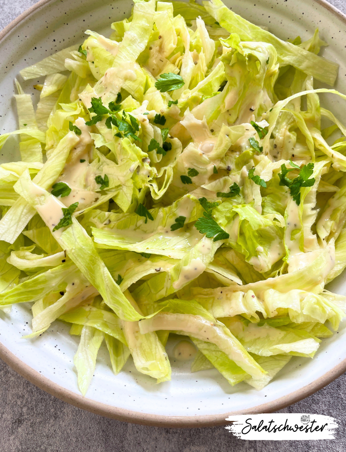 Nahaufnahme eines bunten Tellers mit Eisbergsalat und veganem Joghurt-Knoblauch-Dressing – perfekt für den gesunden Feierabend.