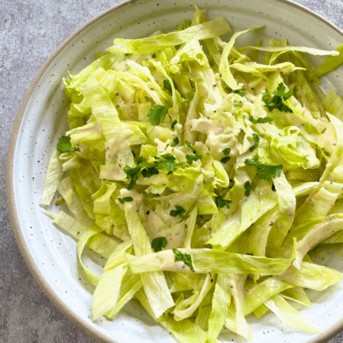 Veganer Eisbergsalat mit Joghurt-Knoblauch-Dressing, serviert als leichter Lunch im Garten – frisch, würzig und schnell zubereitet.