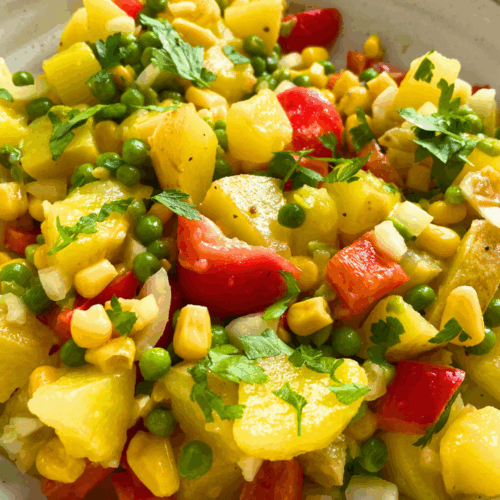 Bunter Kartoffelsalat mit Mais, Erbsen, Paprika und Zwiebeln – servierfertig auf einem Holztisch mit Kräuterdekoration.