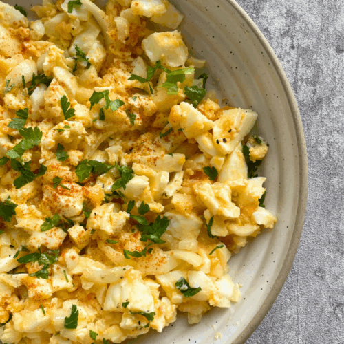 Eiersalat mit Zwiebeln und Öl auf einem weißen Teller angerichtet, serviert mit frischer Petersilie
