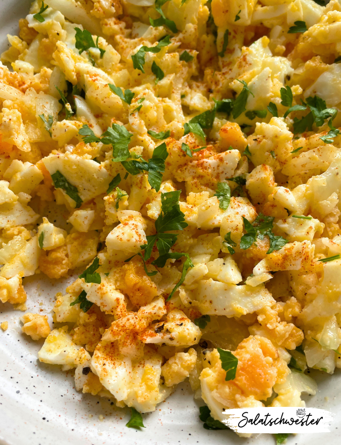Nahaufnahme eines cremigen Eiersalats mit Zwiebeln und Öl, garniert mit frischen Kräutern