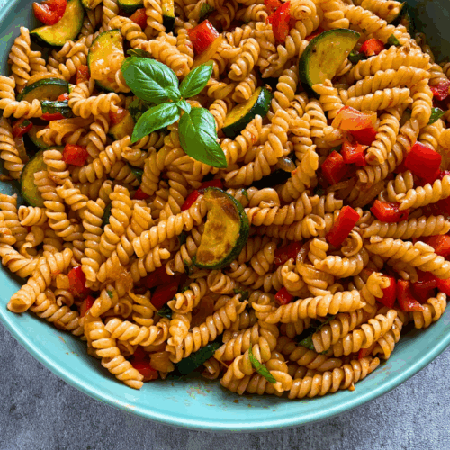 Bunter Nudelsalat mit gebratenen Zucchinischeiben, Paprika und Pesto Rosso, garniert mit frischem Basilikum.