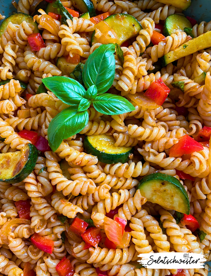 Frischer vegetarischer Nudelsalat mit Pasta, Zucchini, Paprika und aromatischem Pesto Rosso, serviert in einer weißen Schüssel.