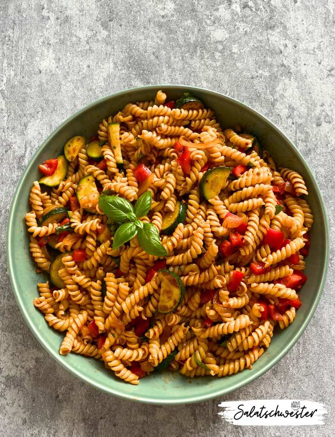 Nudelsalat mit Zucchini und Pesto Rosso, zubereitet mit gebratenen Zwiebeln und frischem Basilikum, perfekt als sommerliche Beilage.