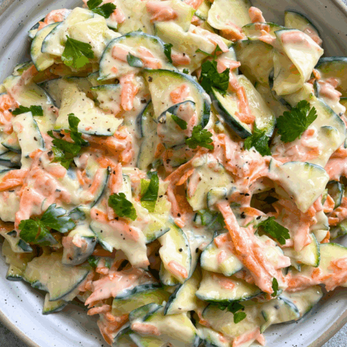 Zucchini-Karotten-Salat mit Joghurtdressing auf einem weißen Teller serviert – frisch, vegan und sommerlich leicht.