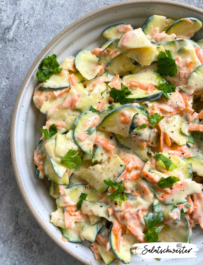 Nahaufnahme eines bunten Zucchini-Karotten-Salats mit cremigem Joghurtdressing und frischen Kräutern.