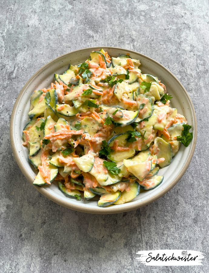 Frischer Zucchini-Karotten-Salat mit Joghurtdressing auf einem Holztisch – perfekt für den Sommer.