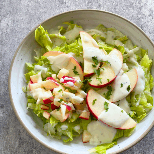 Nahaufnahme von Eisbergsalat mit Apfel und Joghurtdressing, garniert mit frischen Kräutern – eine fruchtige Salatidee für vegane Küche.