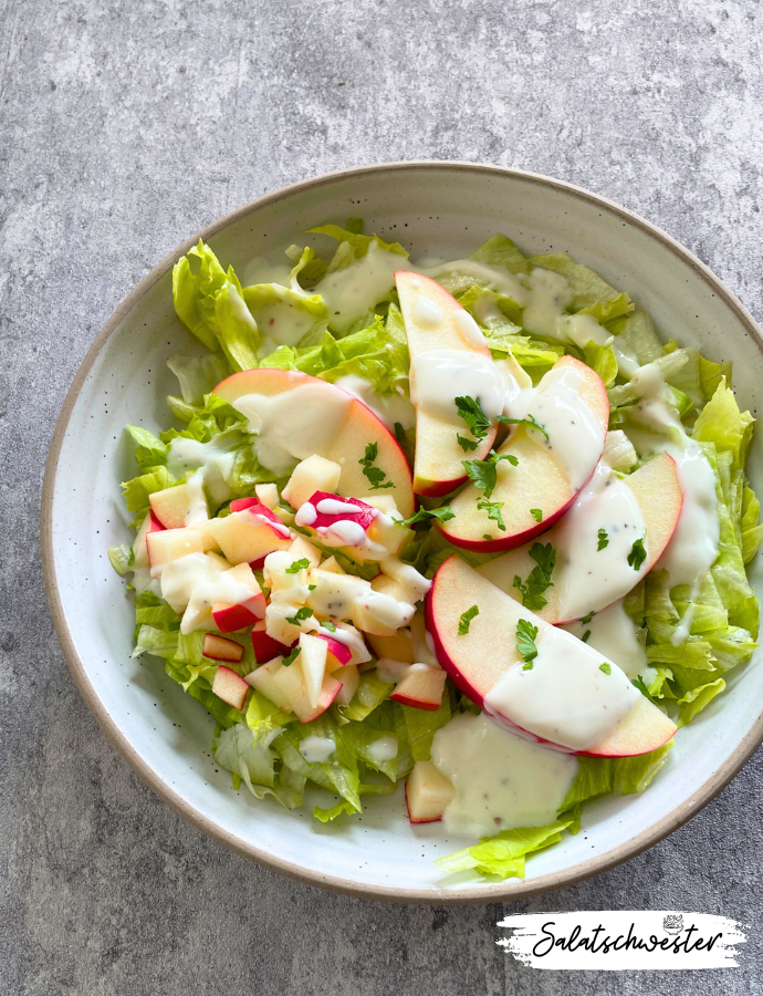 Nahaufnahme von Eisbergsalat mit Apfel und Joghurtdressing, garniert mit frischen Kräutern – eine fruchtige Salatidee für vegane Küche.