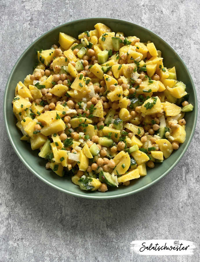 Kartoffelsalat mit Kichererbsen und Gurke auf rustikalem Teller angerichtet