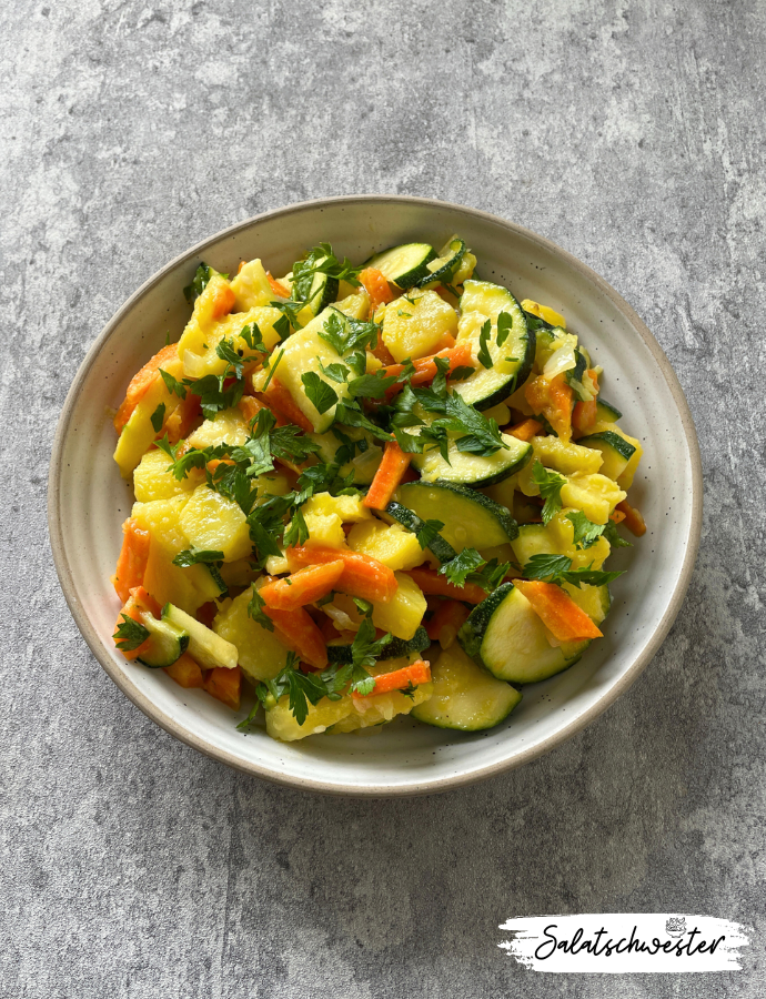 Bunter Kartoffelsalat mit Möhrenstreifen und Zucchinischeiben auf einem Teller serviert.