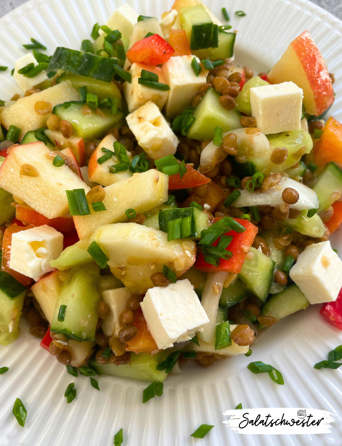 Gesunder Linsensalat mit Gurke, Paprika und cremigem Feta auf einem Holztisch