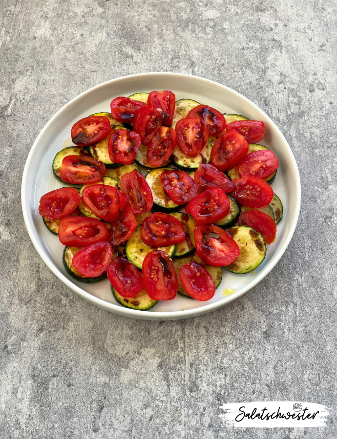 Bunter Zucchinisalat mit Tomaten und gebratenen Zwiebeln auf einer Salatplatte, garniert mit frischen Kräutern