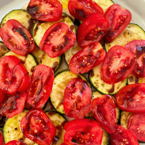 Sommerlicher Zucchinisalat mit Tomaten, Zwiebeln und Granatapfel-Dressing, serviert auf einem weißen Teller