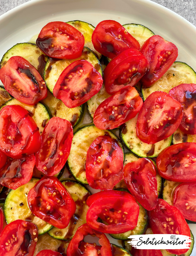 Sommerlicher Zucchinisalat mit Tomaten, Zwiebeln und Granatapfel-Dressing, serviert auf einem weißen Teller