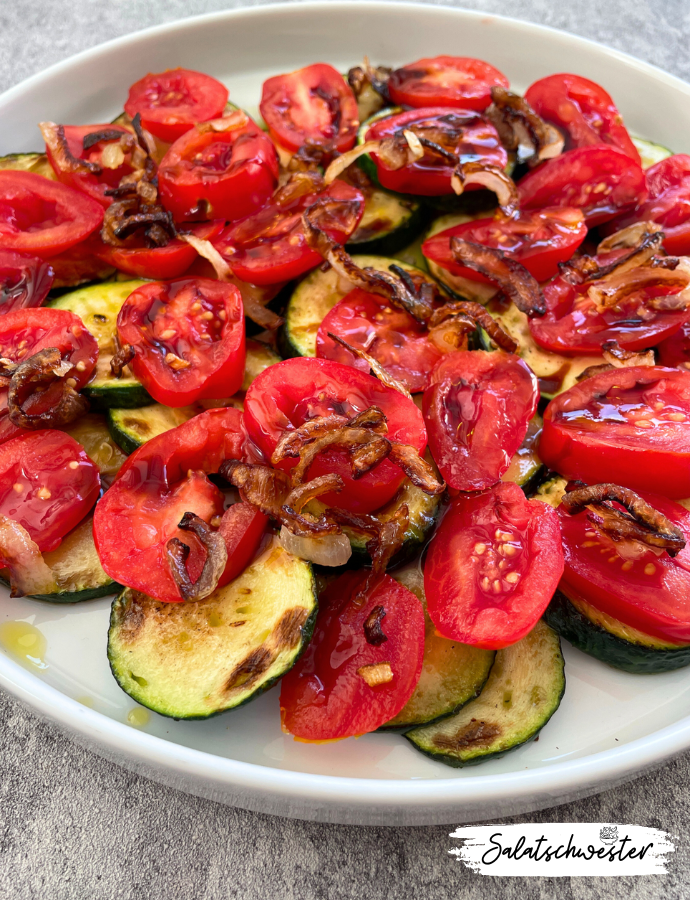 Frischer Zucchinisalat angerichtet mit Tomatenscheiben, gebratenen Zwiebeln und Granatapfelsirup
