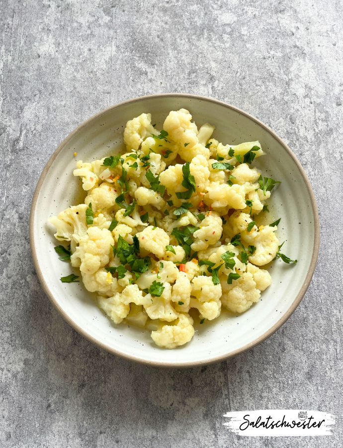 Blumenkohlröschen mit Kräutern und Dressing angerichtet.